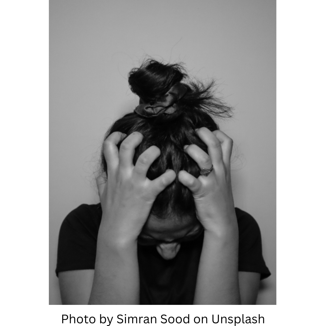 Photo by Simran Sood on Unsplash This picture represents the anger, frustration, and even fury that can be exacerbated by the Wood Element of Spring. It's a black and white photo showing a young woman with a black shirt and her hair in a messy bun. She has her head down and is grabbing her hair with both hands. The tension in her bent fingers show how hard she is gripping.